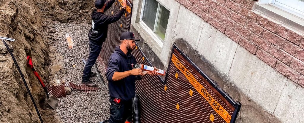Travailleurs installant une membrane d’imperméabilisation sur une fondation résidentielle.