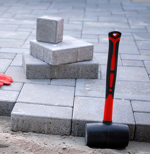 Installation de pavé uni avec maillet de caoutchouc sur une surface résidentielle préparée.