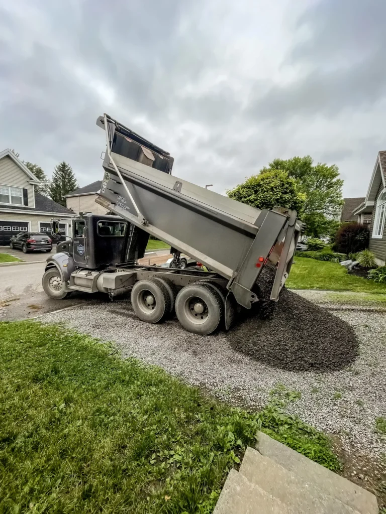 Camion benne déchargeant du gravier concassé dans une allée résidentielle par temps nuageux
