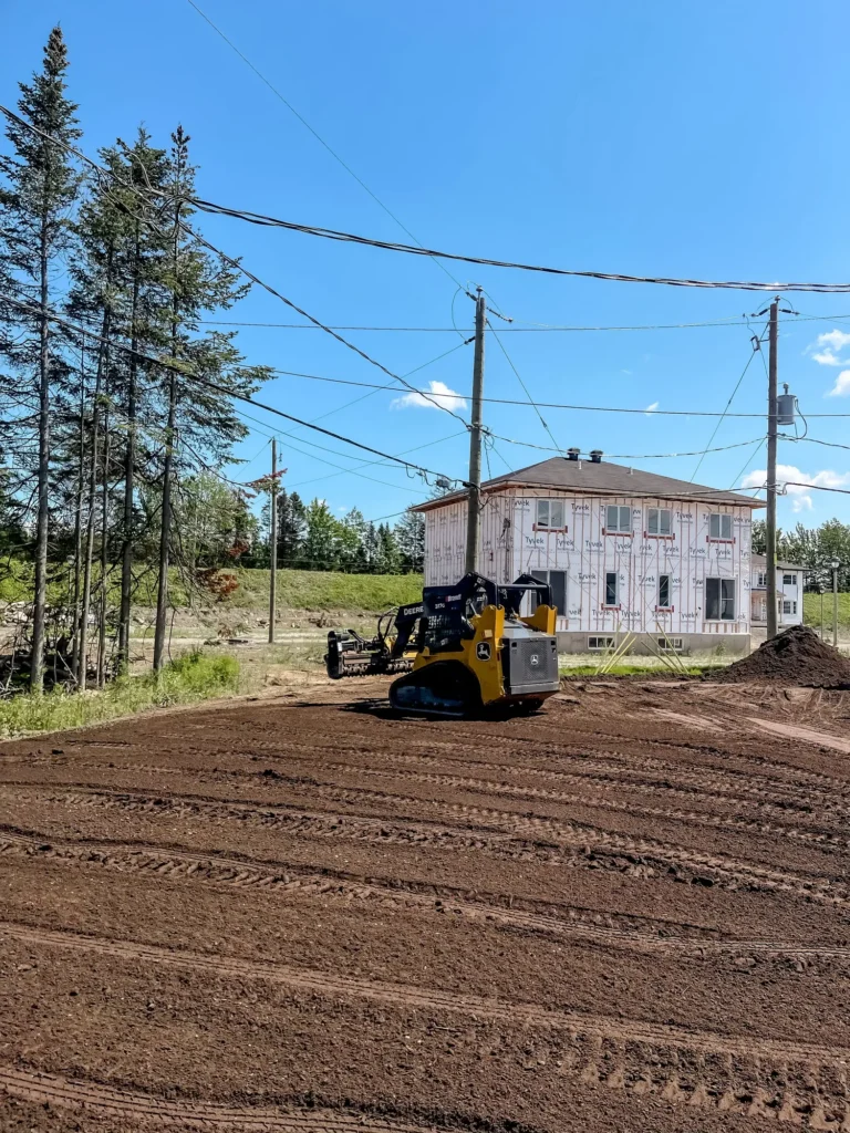 Chargeuse compacte John Deere 317G nivelant terrain devant maison en construction avec membrane Tyvek