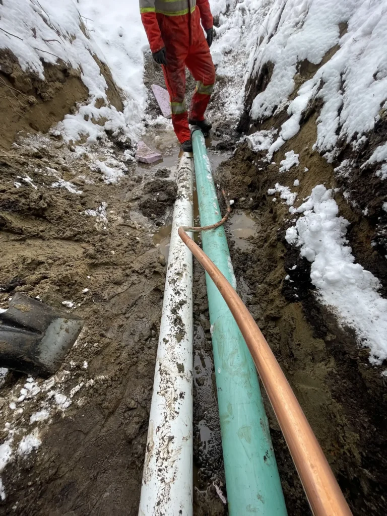 Ouvrier en combinaison rouge sur canalisations dans une tranchée boueuse enneigée en hiver