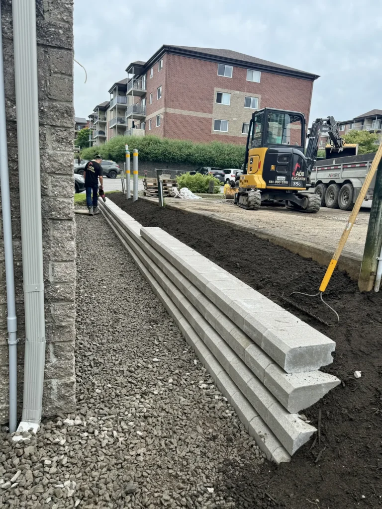 Chantier d'aménagement paysager avec mur de soutènement en blocs de béton et mini-excavatrice ADB Excavation