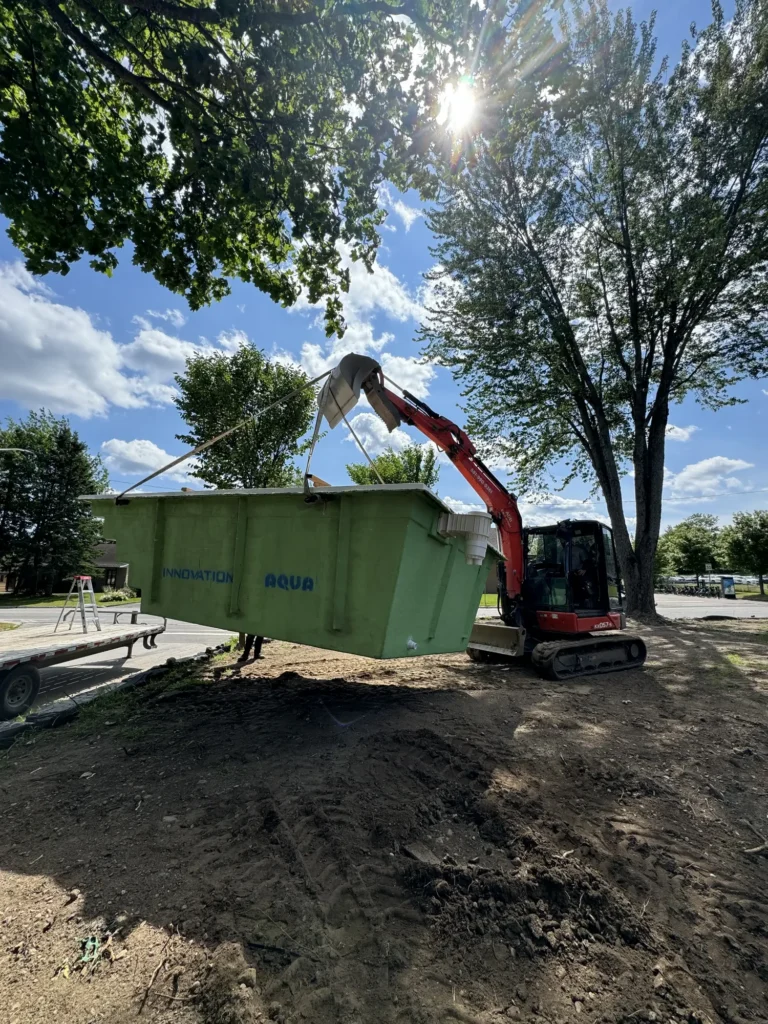 Excavatrice Kubota orange installant une piscine en fibre de verre verte Innovation Aqua sur un chantier