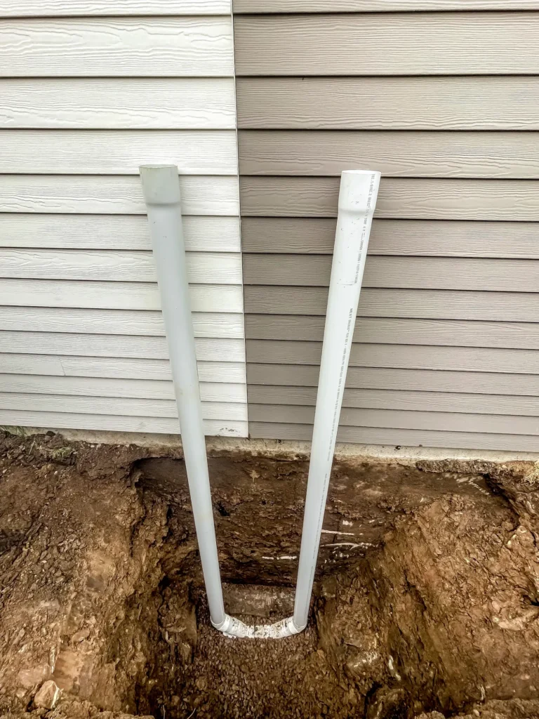 Deux tuyaux PVC blancs installés dans une tranchée creusée le long de la fondation d'une maison pour drainage