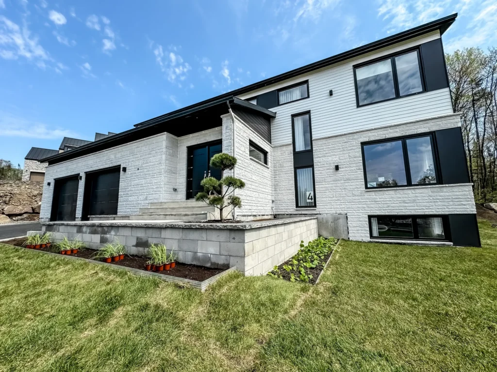 Maison moderne à deux étages avec revêtement de pierre blanche, fenêtres noires et aménagement paysager